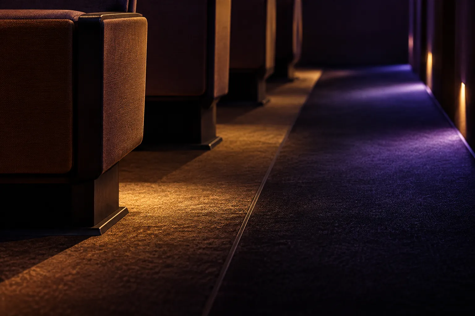 Warm stage light cutting across empty modular seating and a dark aisle.