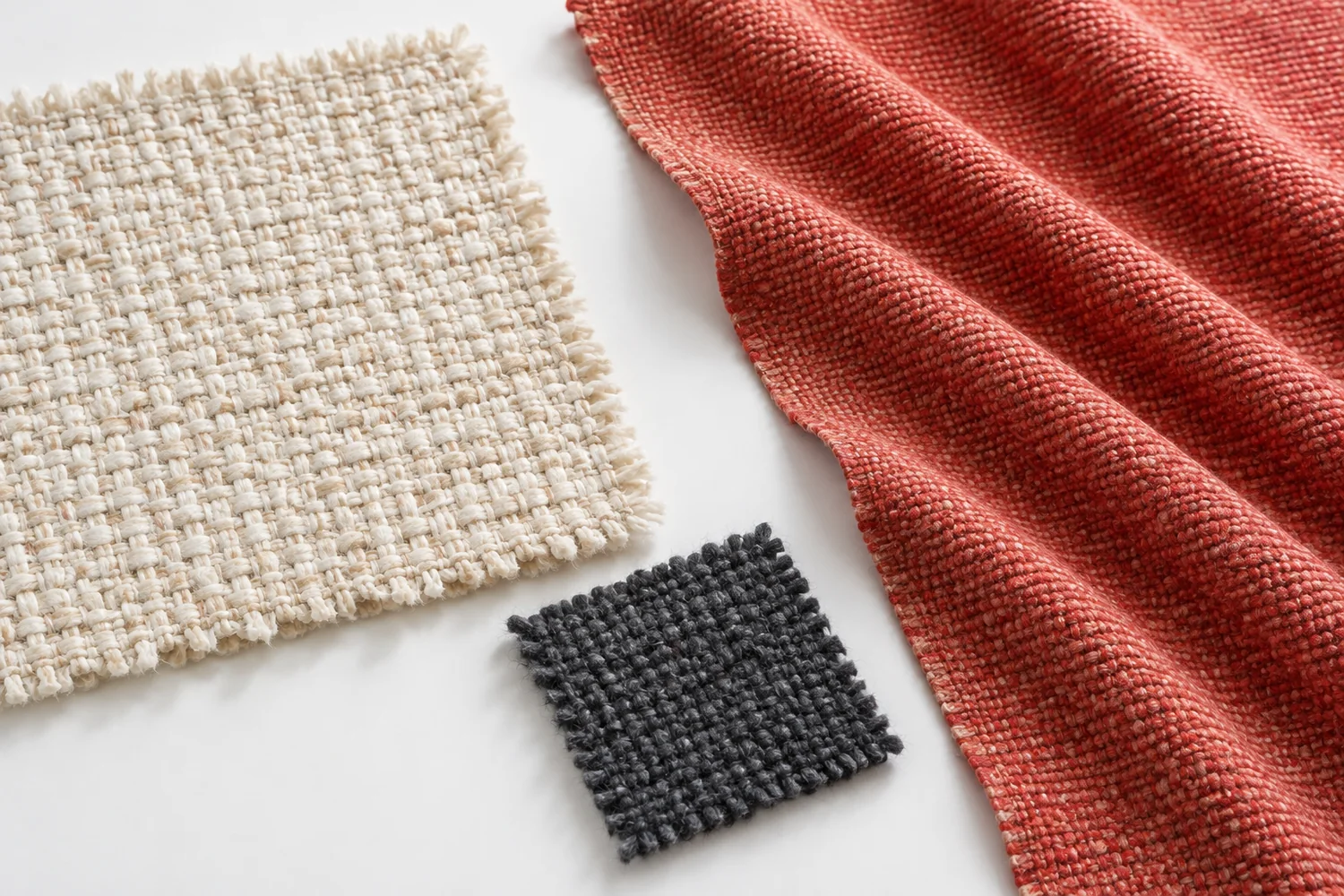 Ivory and charcoal fabric swatches lie beside coral-red cloth in diagonal folds on a white surface.