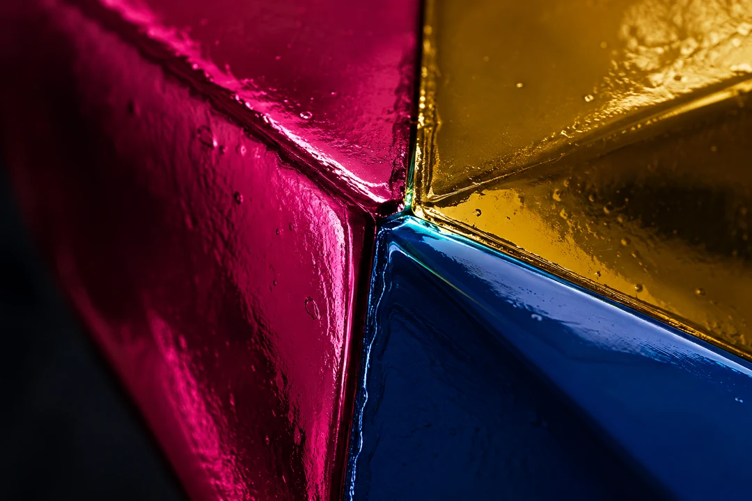 Macro view of a glossy lacquer boundary where magenta, ochre, and blue geometric surfaces meet