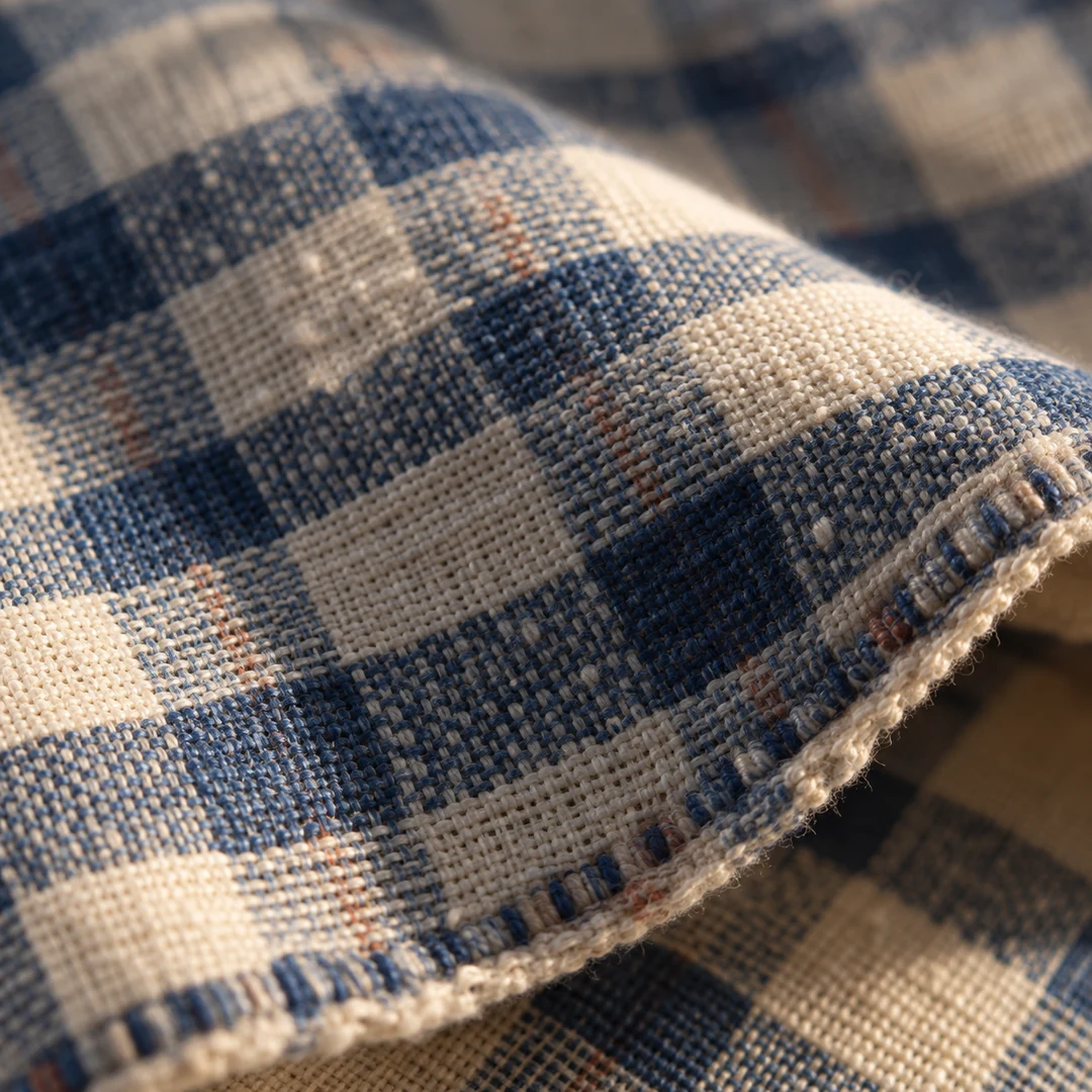 A macro editorial detail of blue and white woven checks showing cotton fibers, crossing threads, and a restrained warm shadow